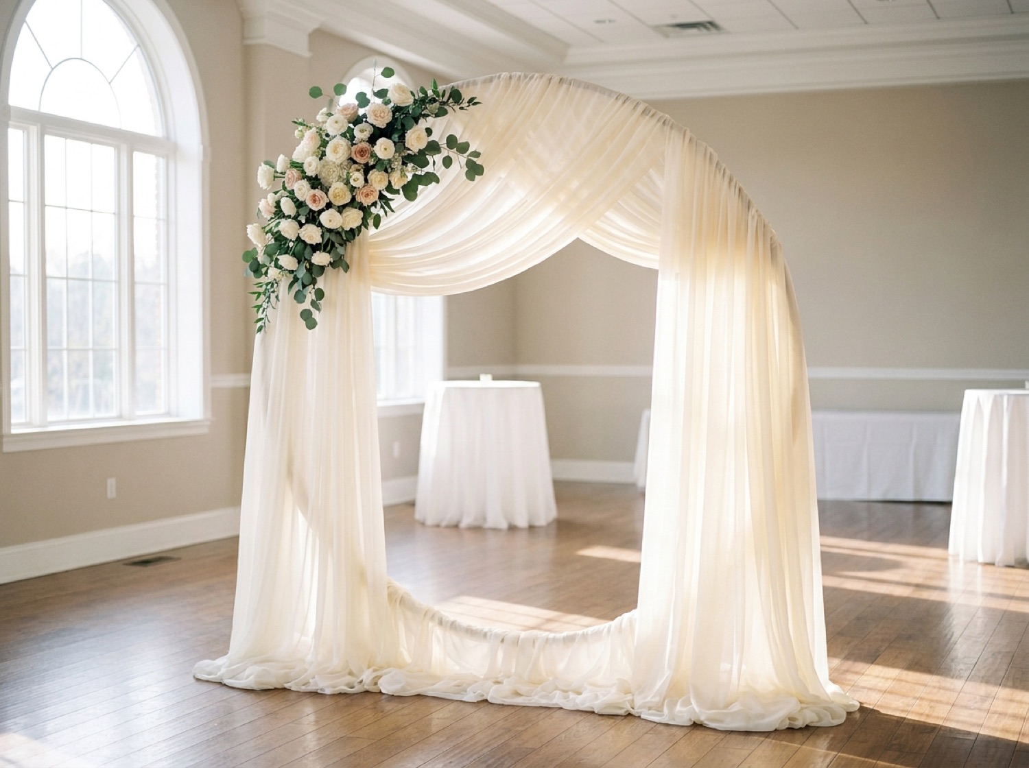 A ceremony arch draped in ivory chiffon with white roses, set up in a Utah reception hall